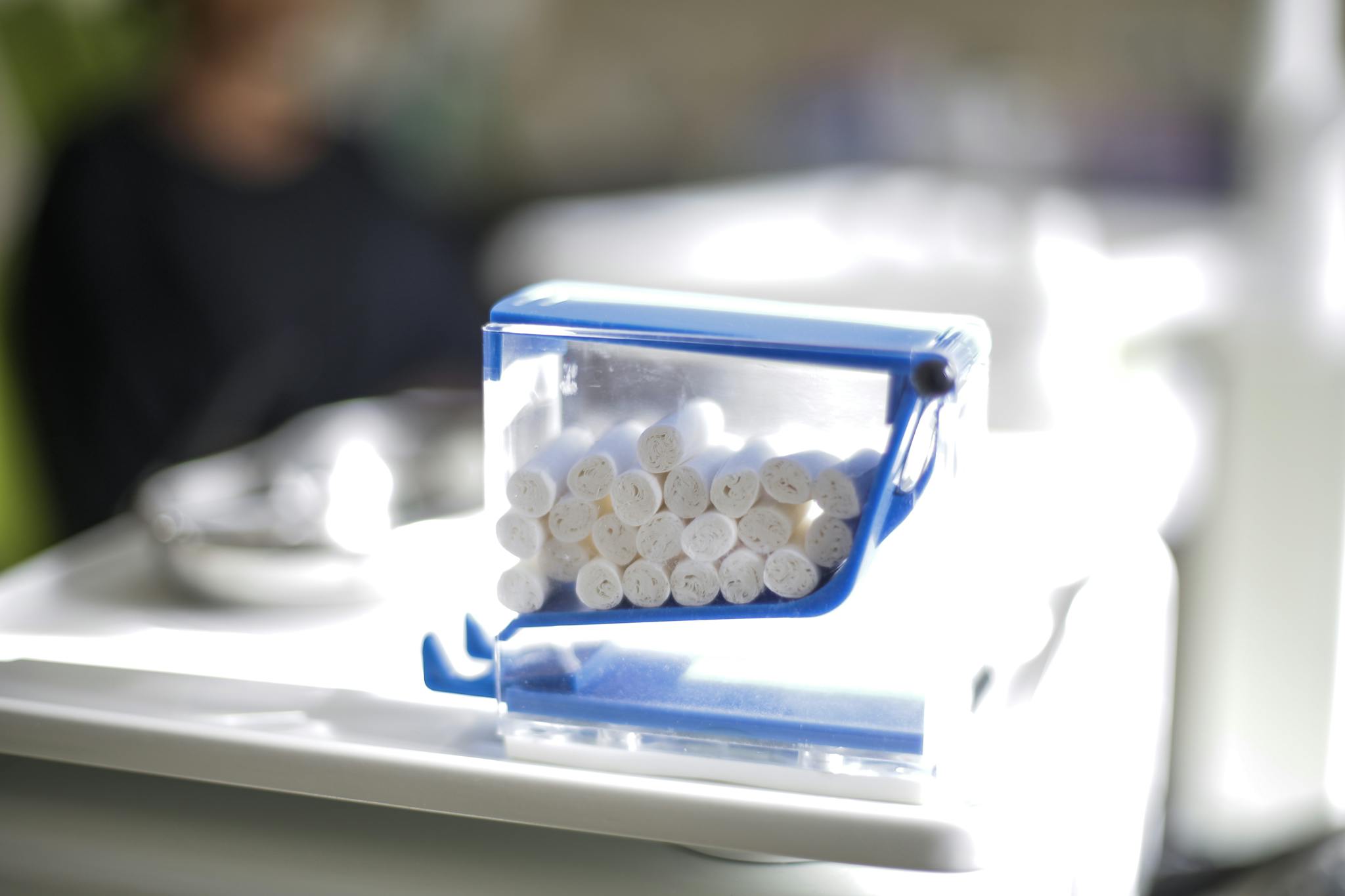 Closeup of set of cotton dental tampons put into transparent plastic box with blue parts located on dental table near dental tray in clinic in sunlight